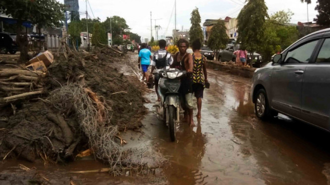 Warga mendorong motor melintasi sisa lumpur akibat banjir bandang di Sentani, Kabupaten Jayapura, Papua, Minggu, 17 Maret 2019.
